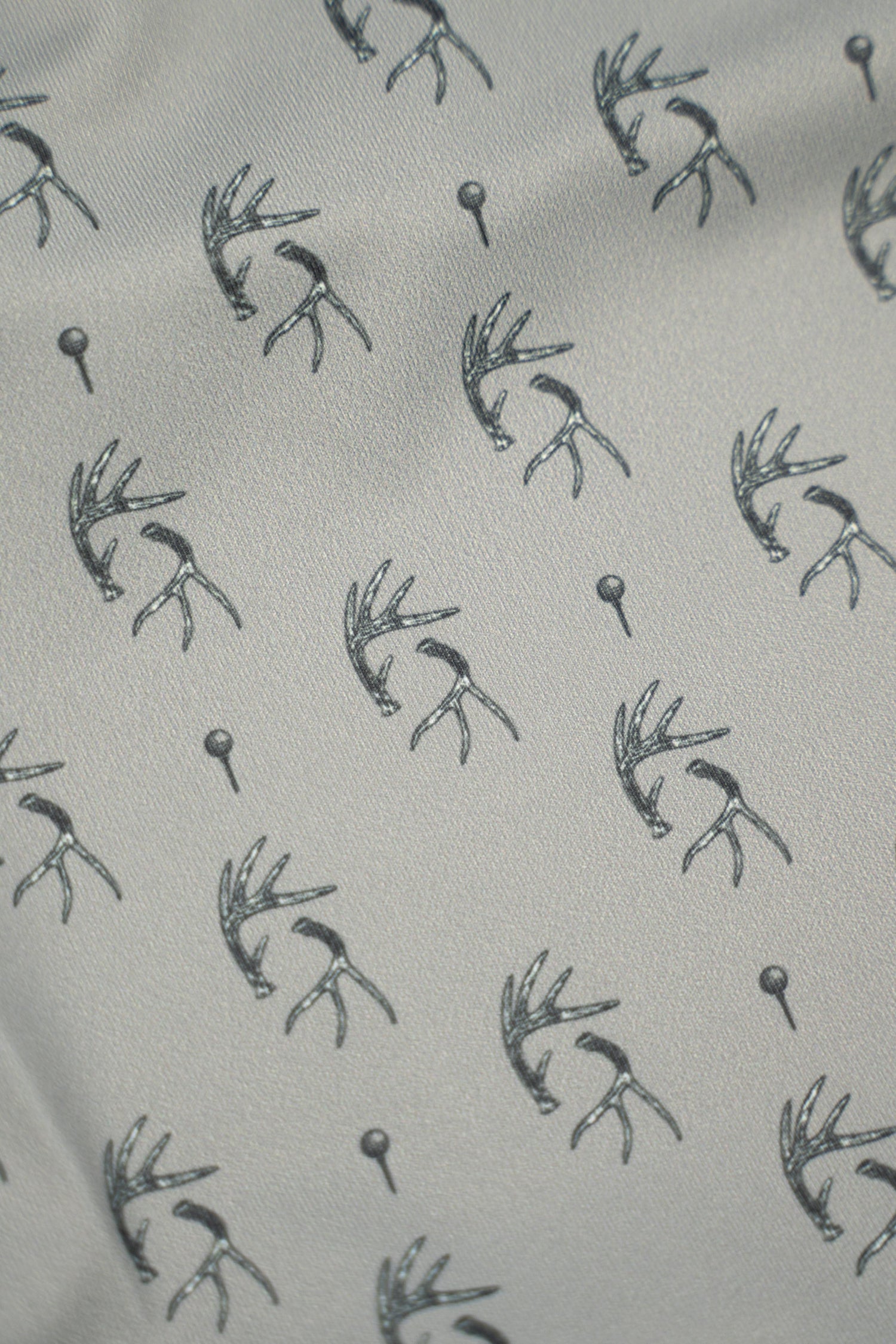 Patterned fabric featuring antlers and golf tees, showcasing the unique design of the Tees &amp; Tines Golf Polo.