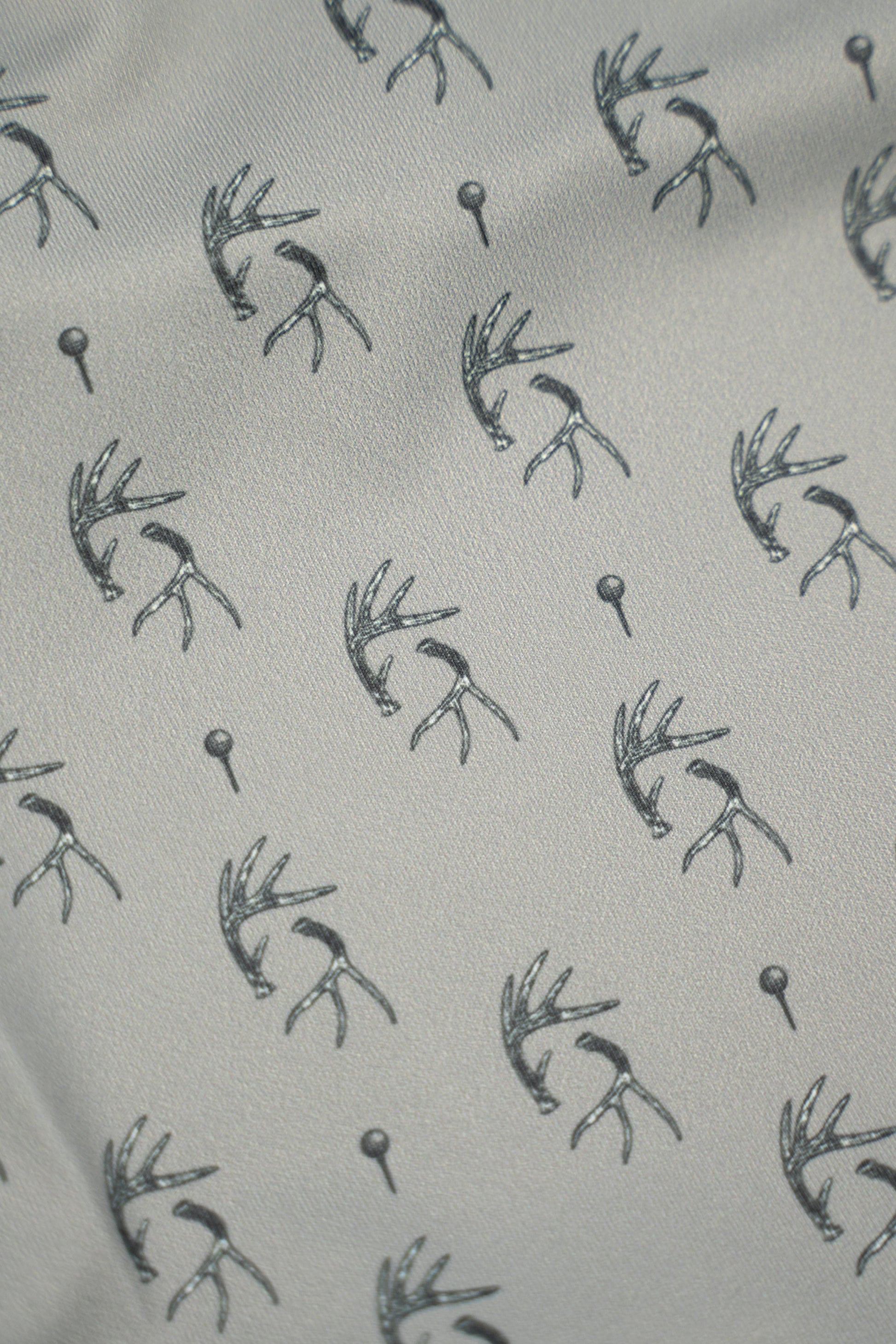 Patterned fabric featuring antlers and golf tees, showcasing the unique design of the Tees & Tines Golf Polo.