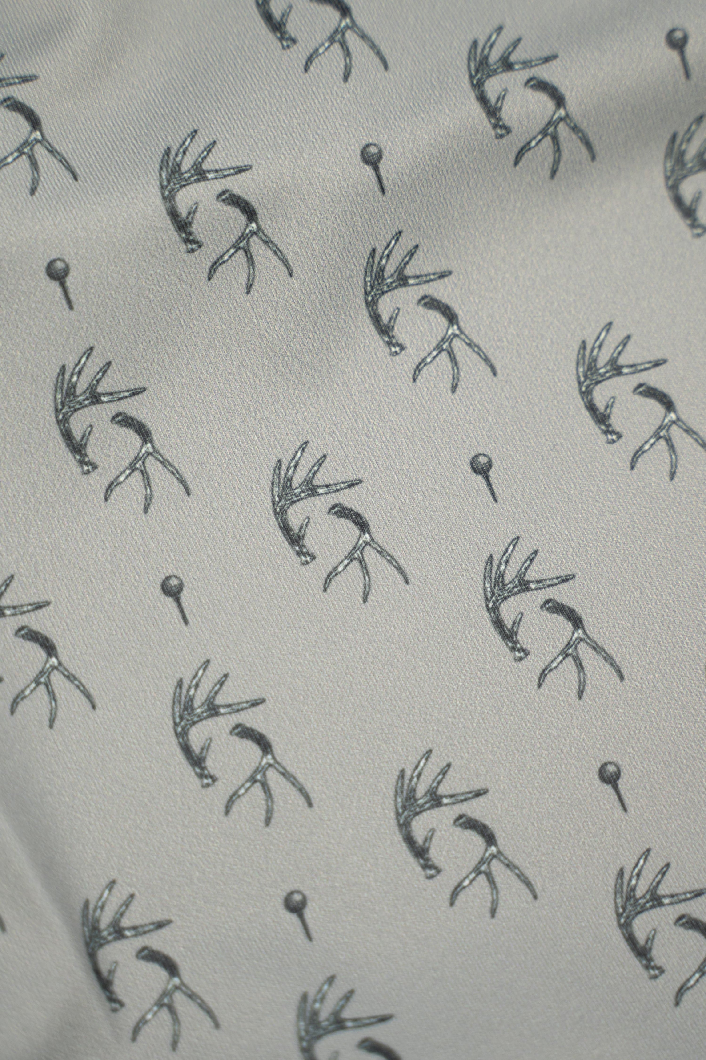 Patterned fabric featuring antlers and golf tees, showcasing the unique design of the Tees &amp; Tines Golf Polo.